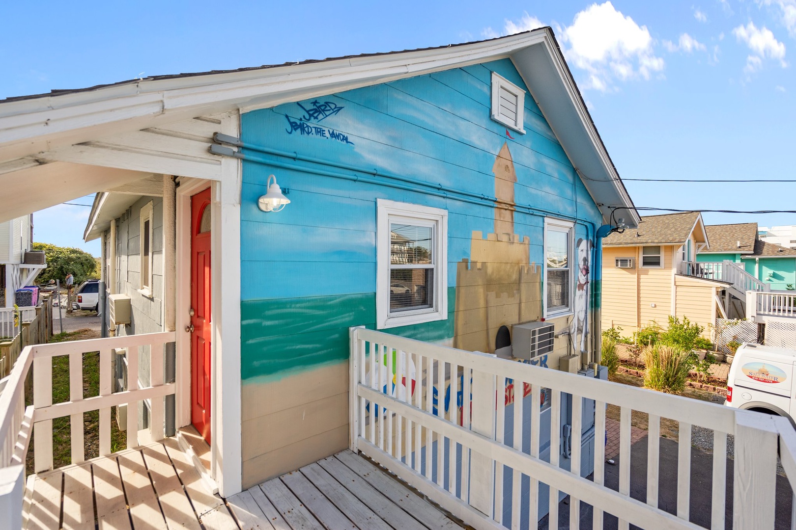 Colorful beach cottage with vibrant ocean-themed mural creates a charming coastal getaway in a friendly neighborhood setting.
