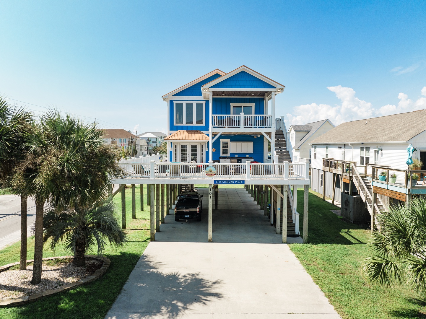 Charming blue beach house on stilts with covered parking and tropical landscaping in a coastal neighborhood.