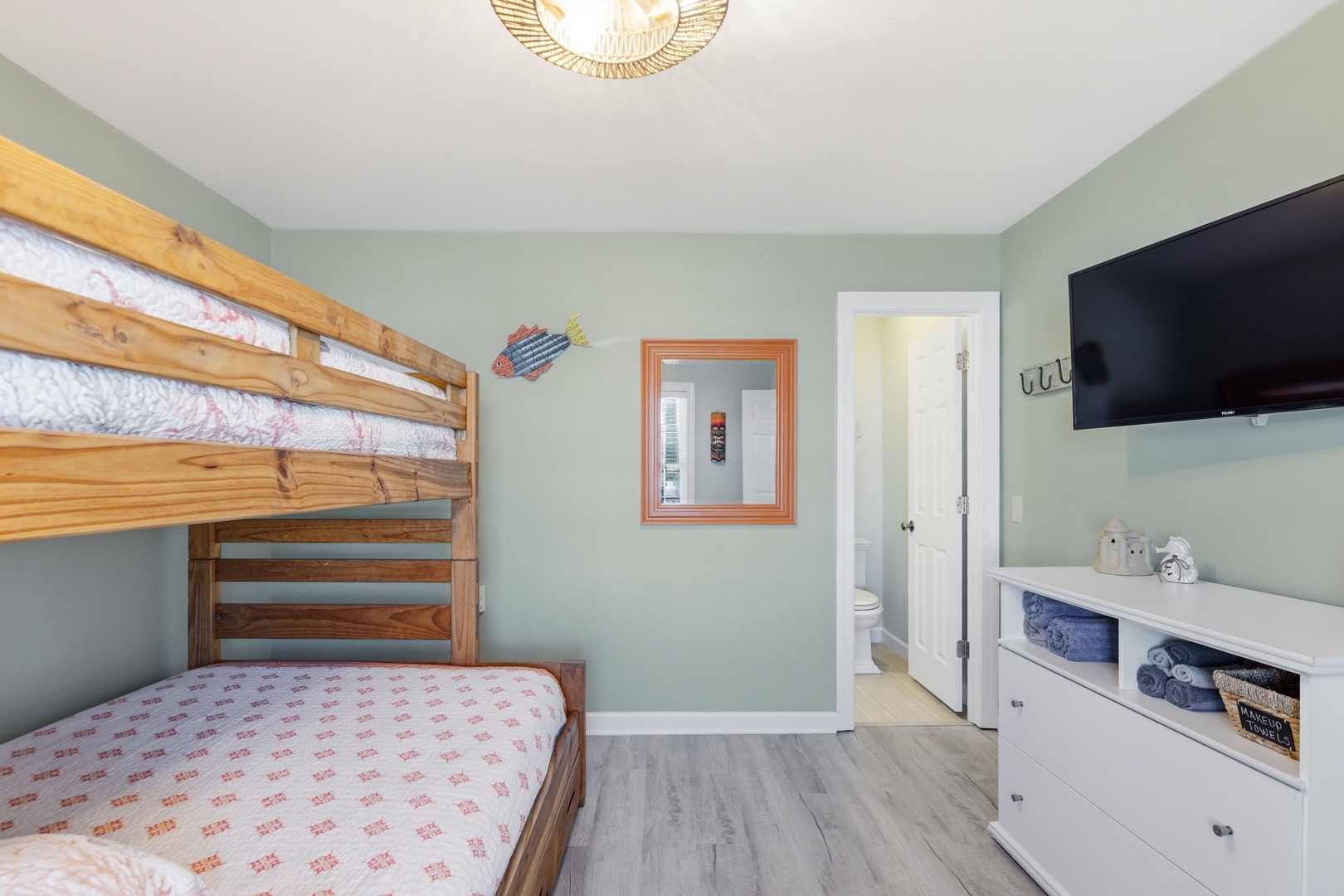 Your space includes a clever bunk bed setup with soft linens, a wall-mounted TV for entertainment, and organized storage—all bathed in calming coastal hues.