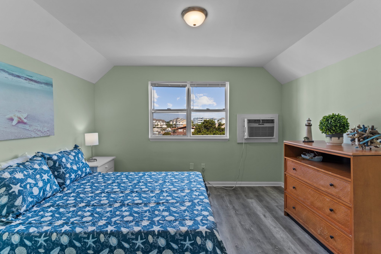 Rest easy in your coastal-themed bedroom with ocean-inspired blue bedding, calming sage walls, and peaceful neighborhood views through your window.