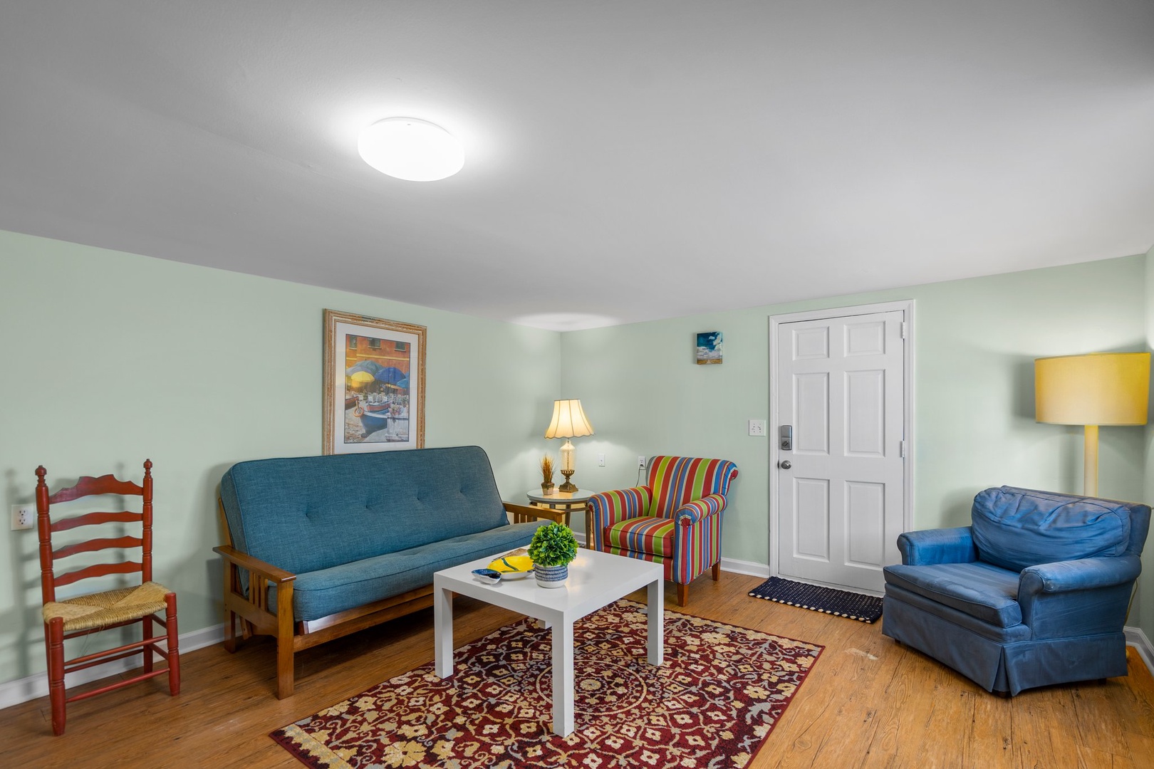 Relax in your cheerful living room with colorful seating, warm wood floors, and charming coastal artwork creating a welcoming retreat.