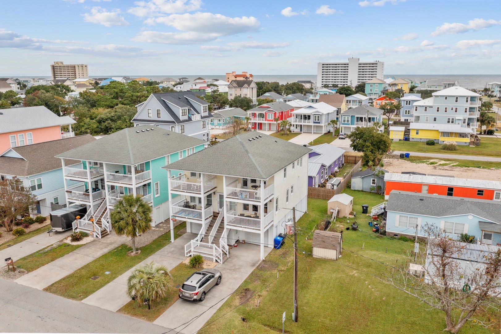 Aerial view showcasing colorful coastal properties in a vibrant beachside neighborhood, with the ocean and city skyline visible in the distance.