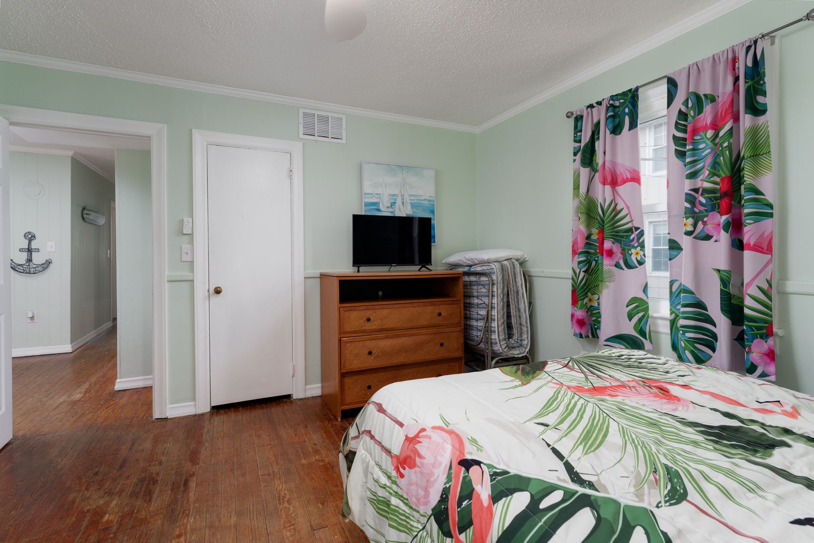 Your tropical-themed bedroom features vibrant flamingo bedding and matching curtains, creating a cheerful oasis with modern amenities and charming hardwood floors.