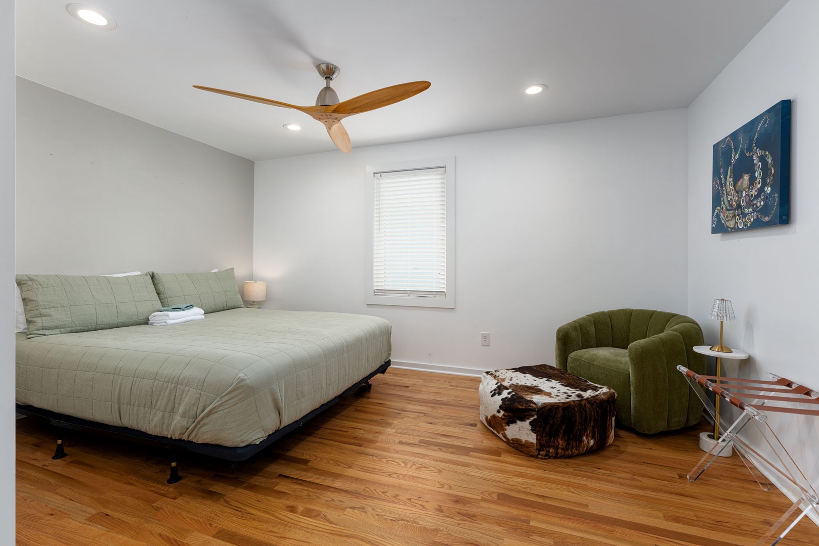 Unwind in your serene bedroom featuring warm wood floors, modern ceiling fan, and stylish green accents that create the perfect retreat.
