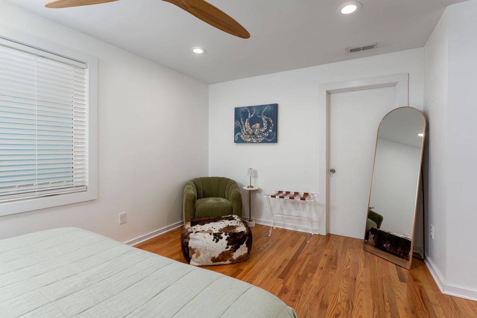 Unwind in your stylish bedroom featuring a cozy reading nook with plush green chair and warm wood floors throughout.
