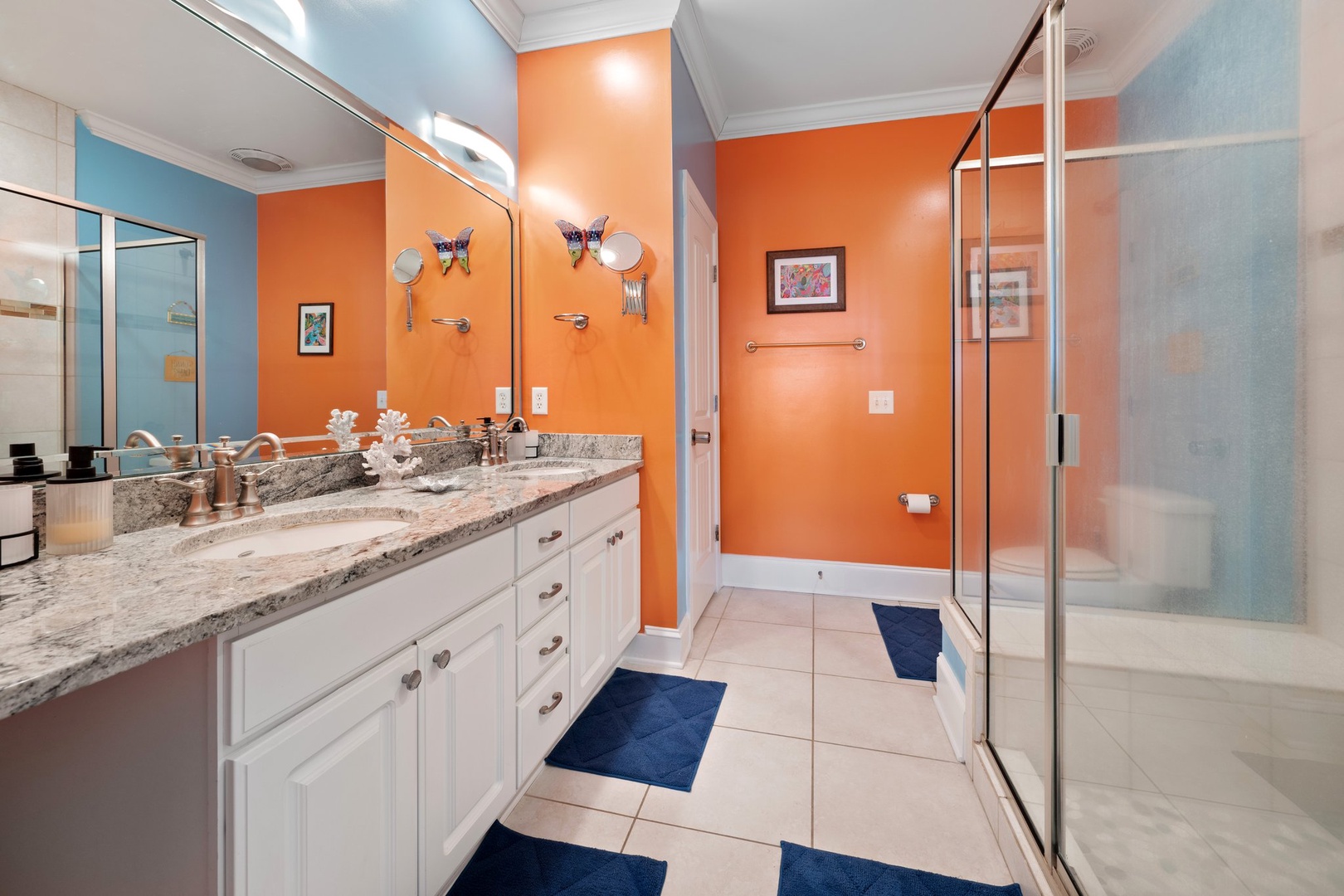 Unwind in your luxurious bathroom featuring vibrant orange walls, granite countertops, and a spacious glass shower perfect for refreshing after beach days.