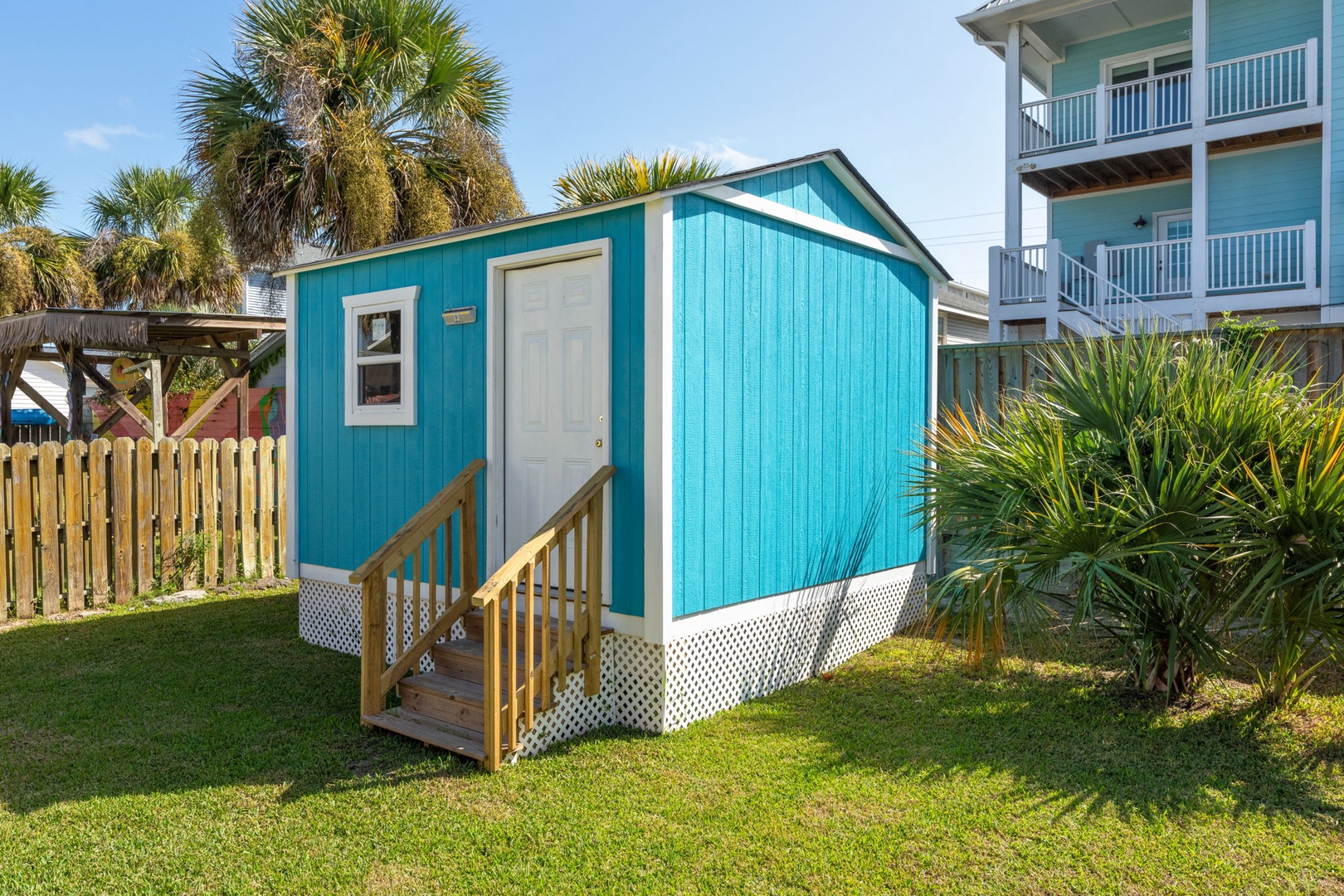 Charming turquoise cottage nestled among tropical palms, offering a unique coastal retreat experience in a peaceful residential setting.
