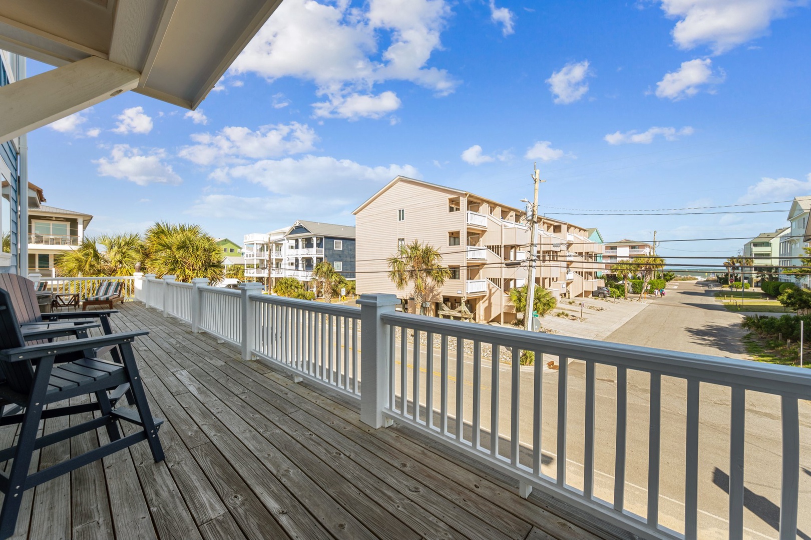 Spacious deck with dining seating offers views of coastal neighborhood and sandy streets leading toward the beach.