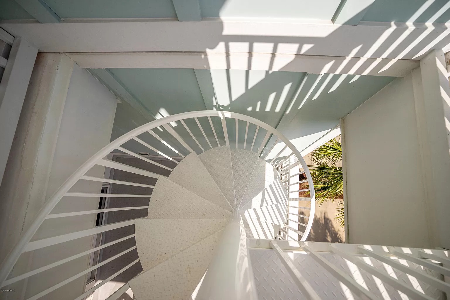 Stunning spiral staircase with white railings creates dramatic shadows in bright natural light, featuring modern architectural design.