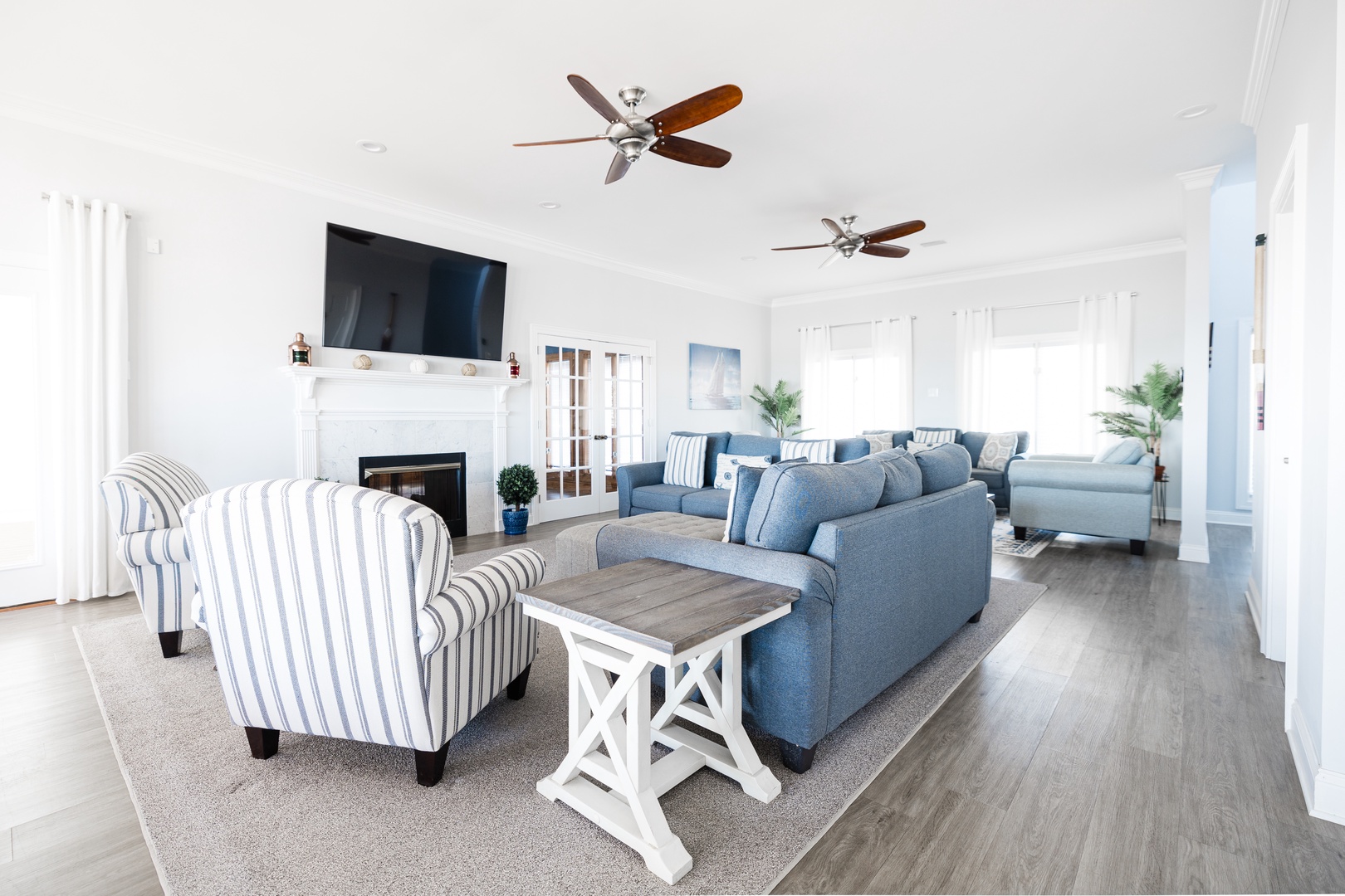 Settle into your stylish coastal retreat with plush blue sofas, striped accent chairs, and a cozy fireplace for perfect relaxation.