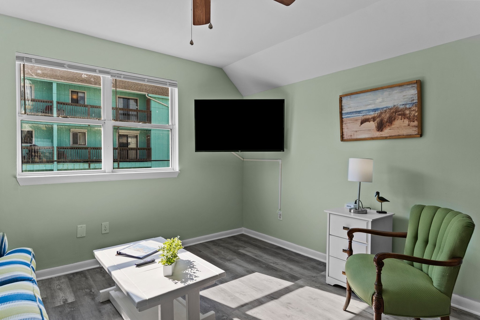 Relax in your peaceful green living room with comfortable seating, modern TV, and charming coastal artwork.