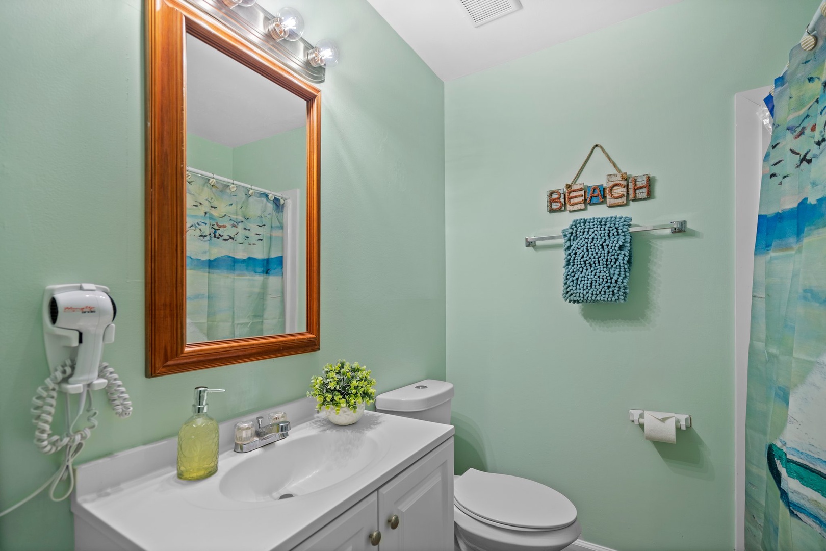 Your coastal-themed bathroom features soothing mint walls, beach decor, and thoughtful amenities like a hair dryer for your convenience.