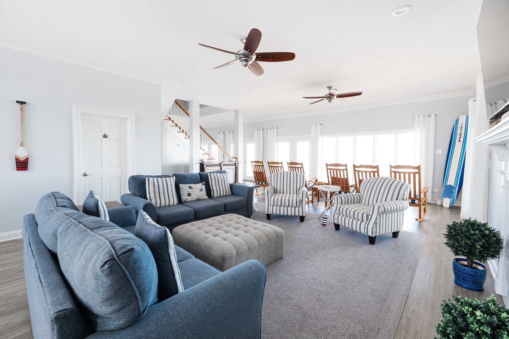 Relax in your spacious living room with comfortable blue sofas, coastal-inspired chairs, and gentle ceiling fans creating the perfect beach house atmosphere.