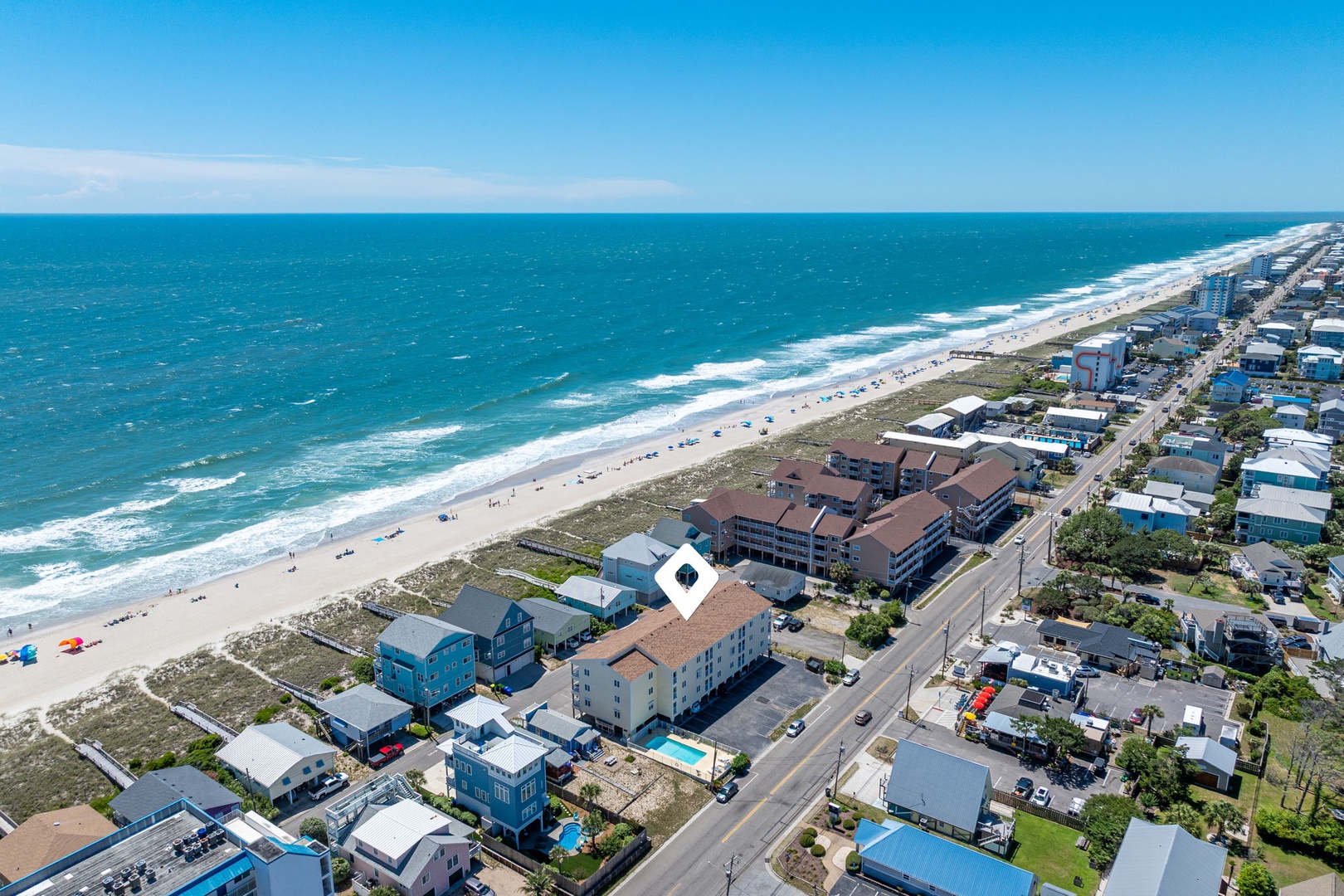 Aerial view of a coastal beachfront neighborhood featuring residential properties, oceanfront accommodations, and sandy shores stretching along the turquoise Atlantic waters.
