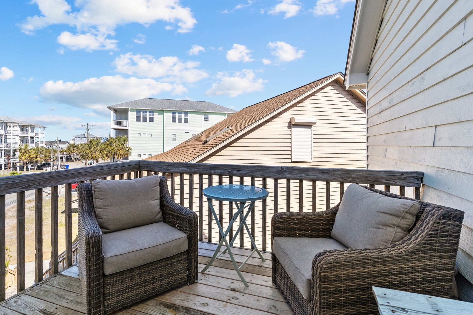 Step onto your private balcony to enjoy morning coffee with coastal neighborhood views and comfortable wicker seating.