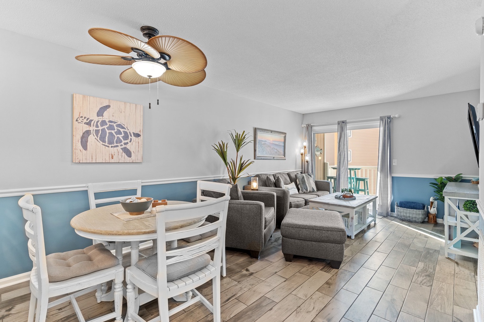 Relax in your coastal-themed living space with comfy sectional seating, beach-inspired decor, and tropical ceiling fan creating the perfect vacation vibe.