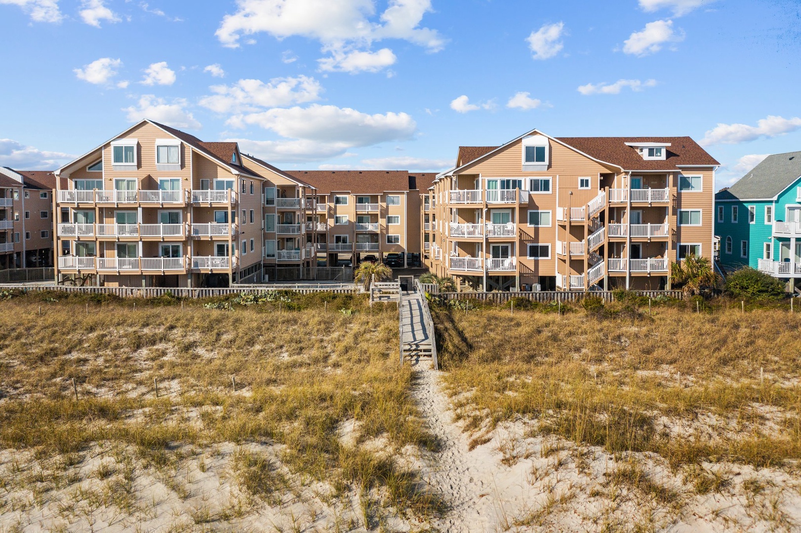 Charming beachfront rental community with direct beach access via sandy boardwalk, featuring multi-level units with private balconies overlooking coastal dunes.