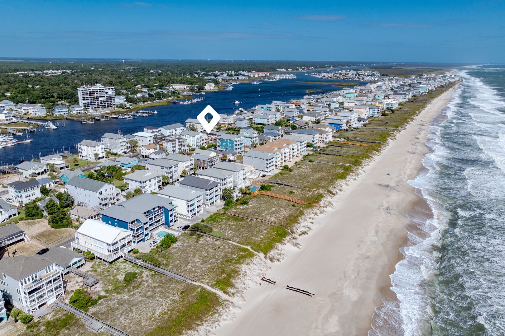 Aerial view of oceanfront community with pristine beach, marina, and vacation homes nestled between bay and Atlantic coastline.