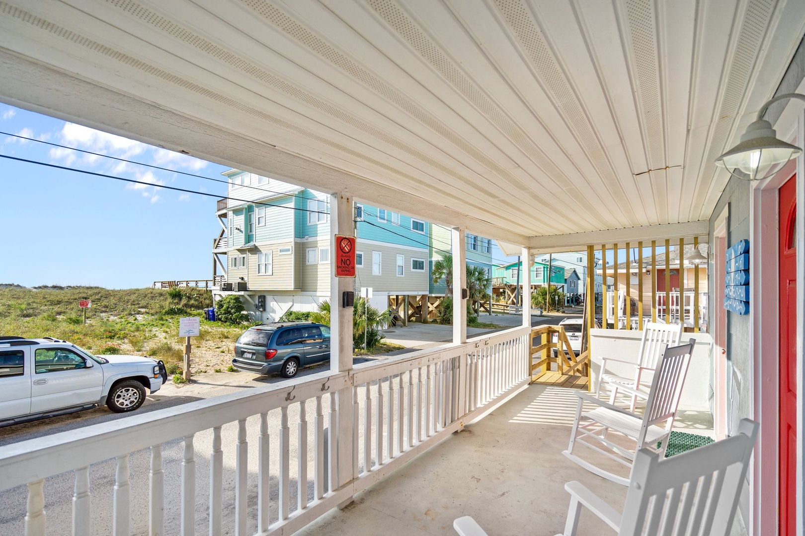 Relax on your covered porch with rocking chairs, enjoying views of colorful beach houses and natural dunes.