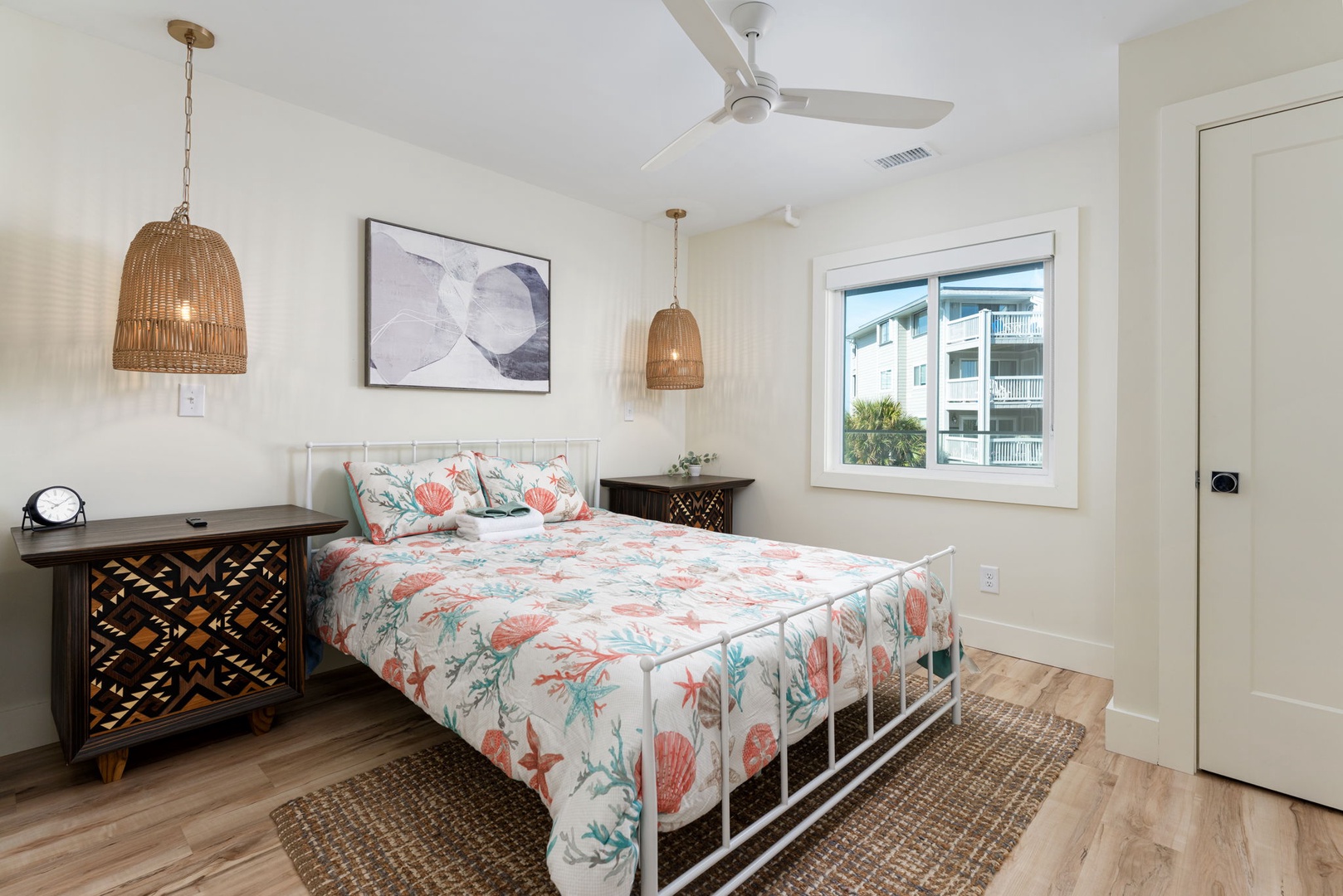 Drift off to sleep in this bright, coastal-inspired bedroom featuring tropical bedding, woven pendant lights, and charming neighborhood views.