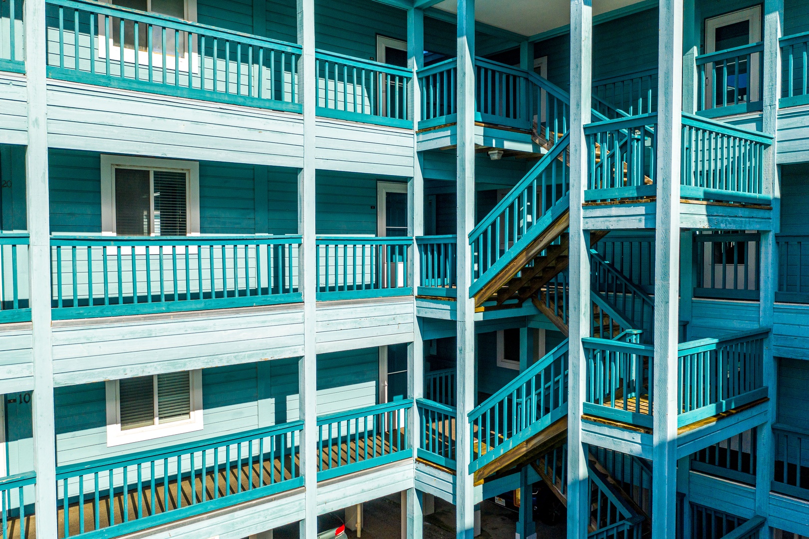 Multi-story property building featuring turquoise-painted balconies and staircases with white wooden railings throughout multiple levels.