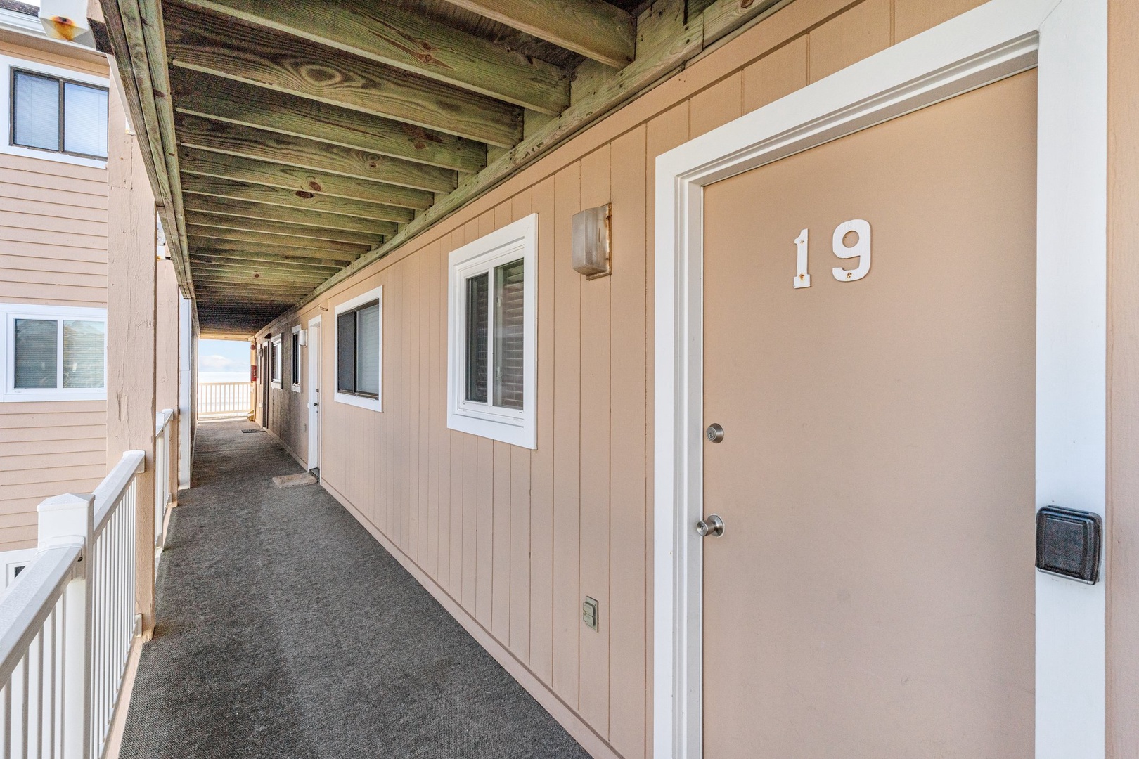 The covered walkway leading to your unit entrance, featuring classic coastal architecture with exposed wooden beams overhead.