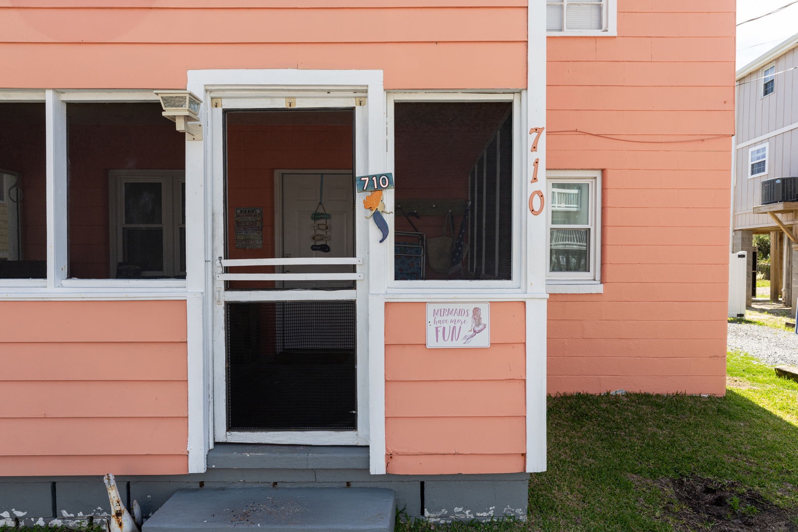Charming coral-painted exterior marks your vacation home's entrance, featuring unit number 710 and a welcoming screened door that opens to your coastal retreat.