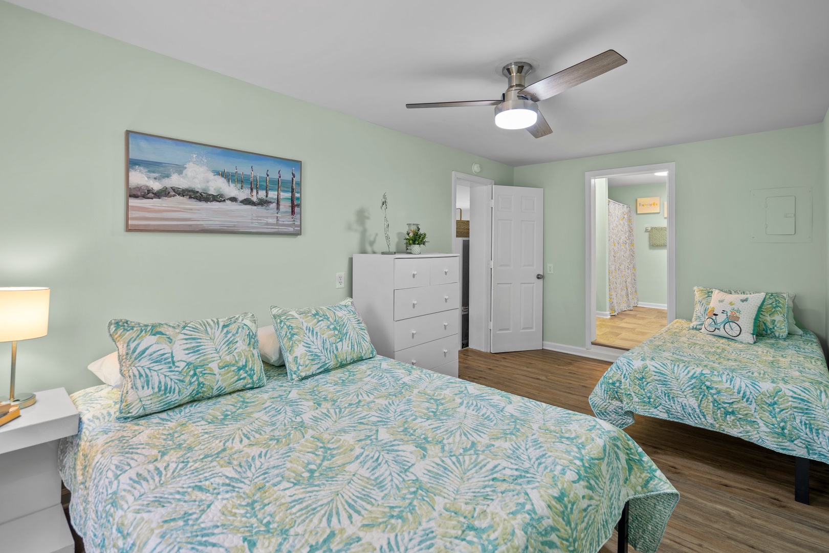 Relax in this bright coastal bedroom with tropical bedding, ceiling fan, and soothing ocean artwork.