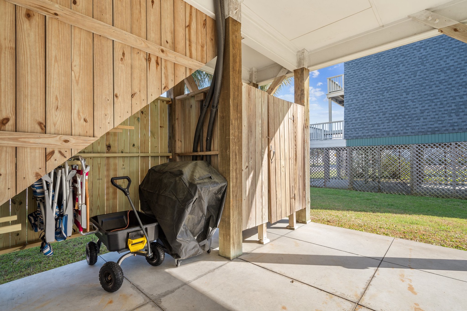 Covered storage area beneath elevated deck with grill and beach equipment for your coastal getaway convenience.