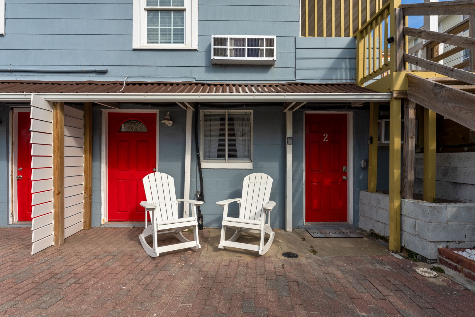 Charming beachside cottage with bright red doors and welcoming white rocking chairs on a private brick patio.