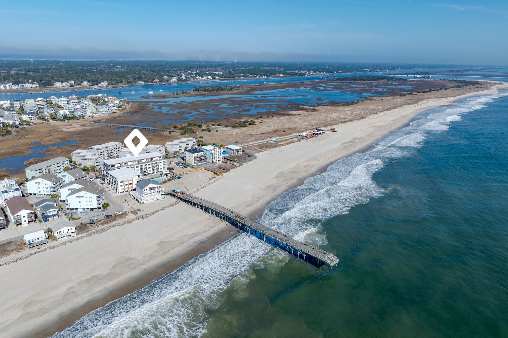 Stunning aerial view of pristine beachfront community with fishing pier extending into turquoise waters along the Atlantic coast.