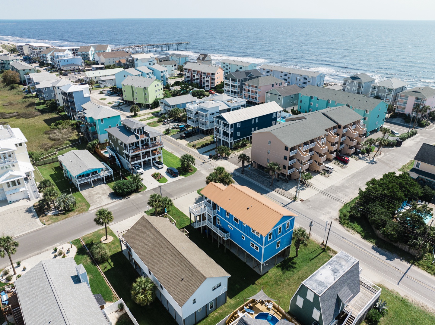 Aerial view of colorful beachfront community with pier extending into the ocean.