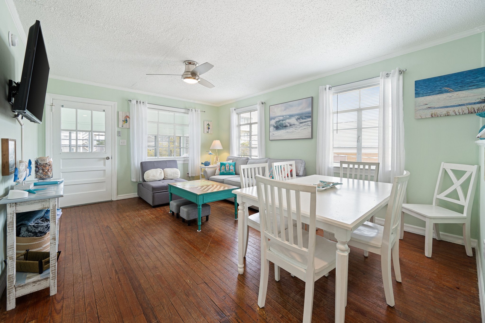 Relax in your coastal-themed living space with charming hardwood floors, comfortable seating, and plenty of natural light streaming through multiple windows.