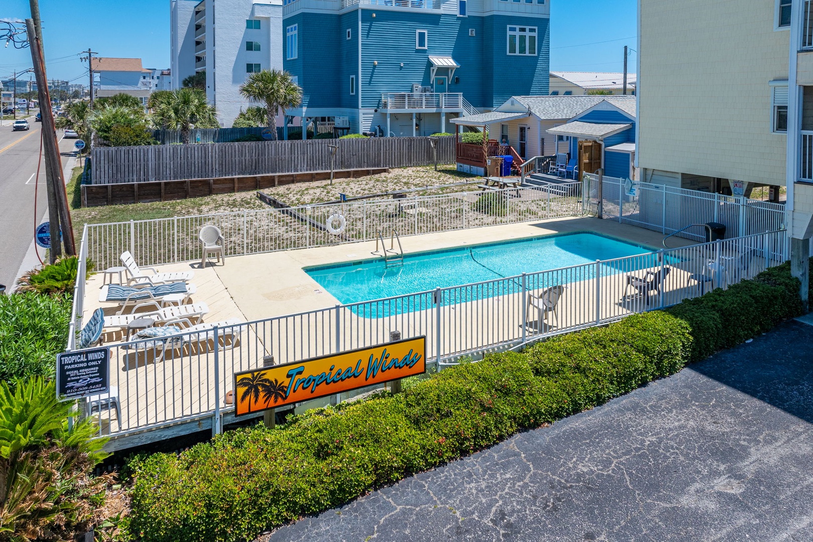 Aerial view of Tropical Winds vacation property featuring a private fenced pool area surrounded by coastal homes in a beachside neighborhood.