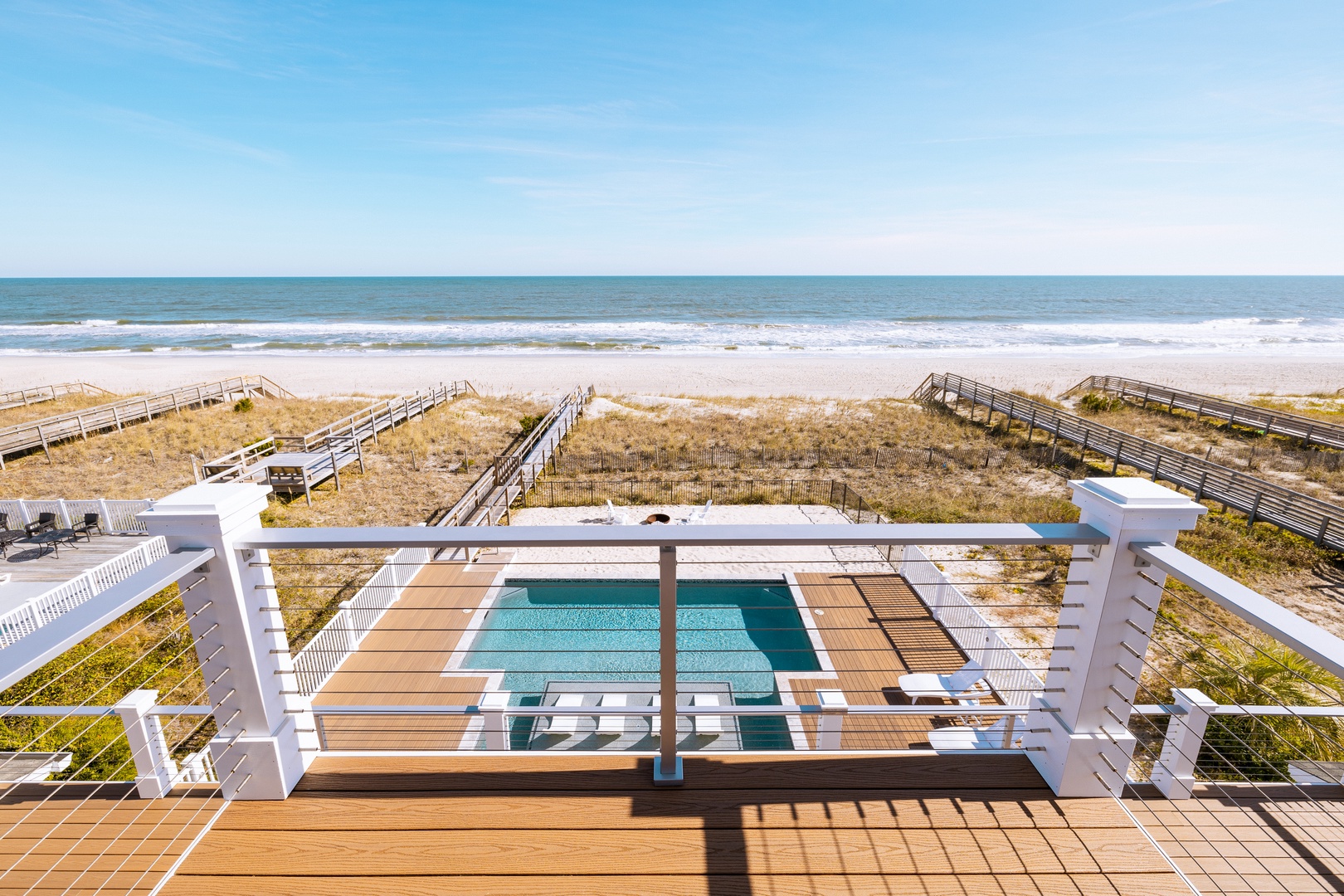 Oceanfront deck with pool and direct beach access via wooden walkways, offering pristine coastal views.