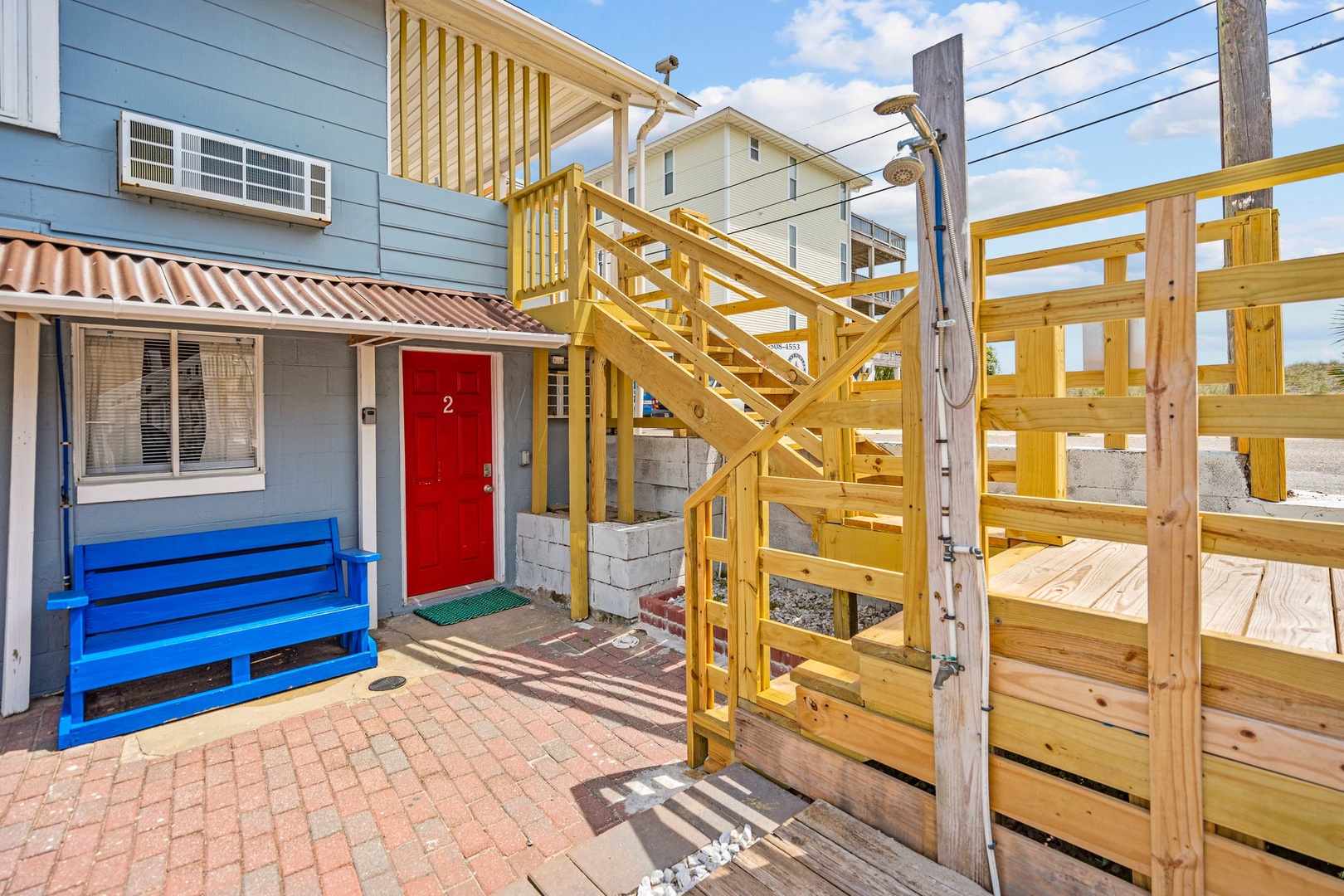 Multi-level beach house with charming red door entrance and wooden deck access in a coastal neighborhood setting.
