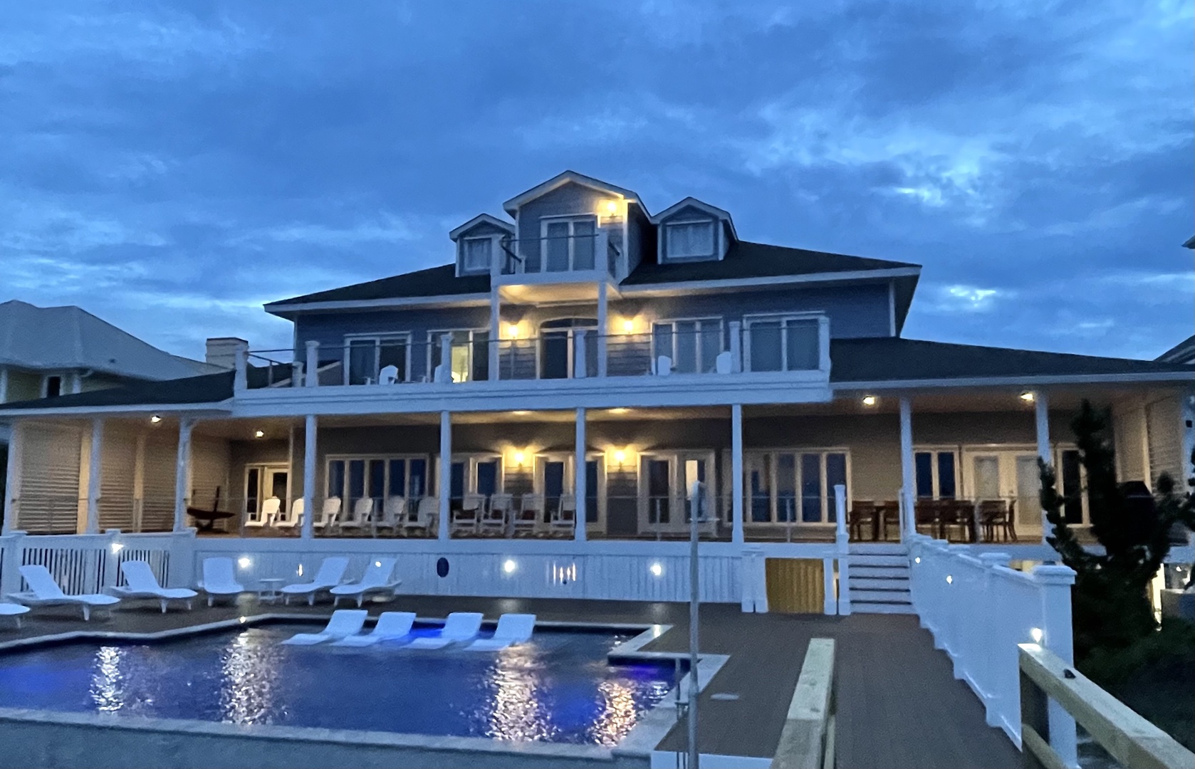 Stunning waterfront estate with illuminated pool and expansive decks creating the perfect evening ambiance for arrival.