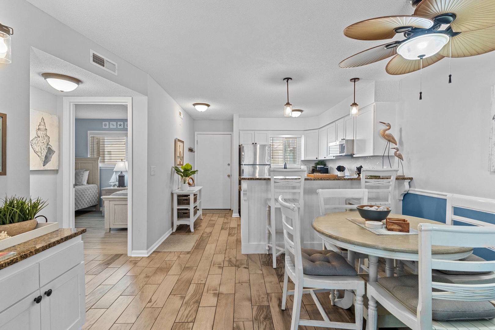 Your bright, coastal-inspired kitchen flows seamlessly into the dining area, with warm wood floors and tropical ceiling fan creating a perfect beachside vibe.