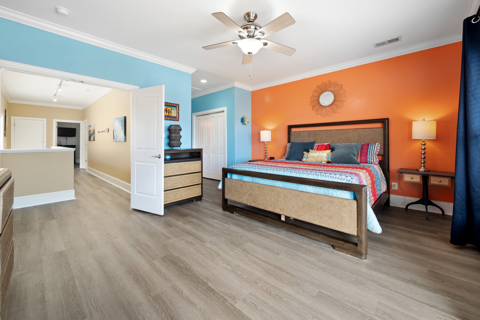Your vibrant bedroom features bold coral and turquoise walls, a king-size bed with coastal linens, and an open layout connecting to your kitchen space.