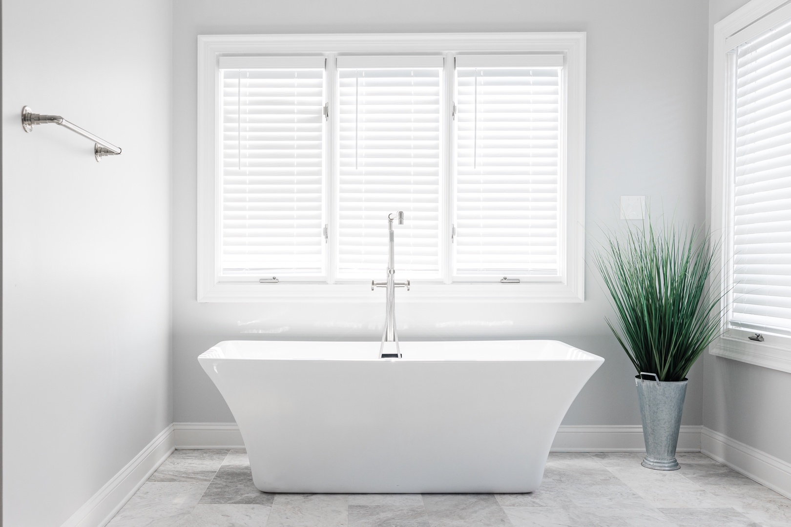 Sink into this sleek freestanding tub for a luxurious soak, surrounded by bright natural light and serene white shutters for your ultimate relaxation.