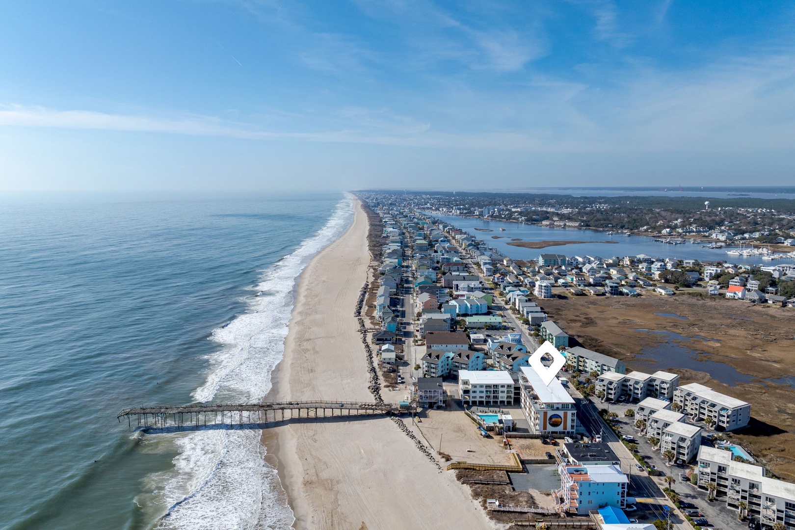 Stunning aerial view of pristine coastline with expansive beaches, charming pier, and vibrant coastal community nestled between ocean and bay waters.