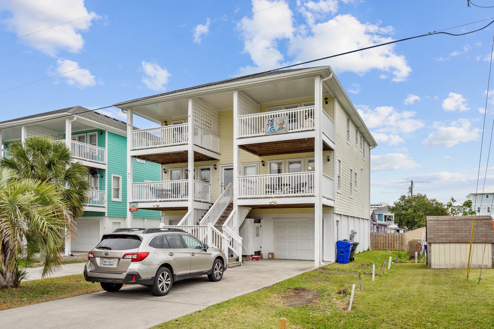Bright coastal home with covered parking and multiple balconies in a tropical neighborhood setting.