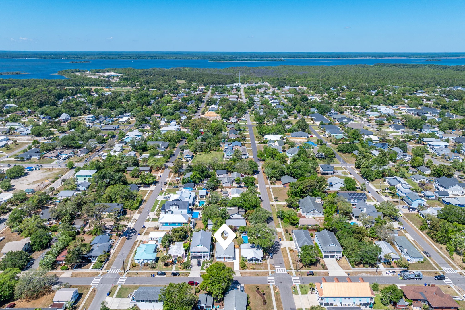 Aerial view of a coastal community with tree-lined streets, residential neighborhoods, and pristine blue waters stretching to the horizon.