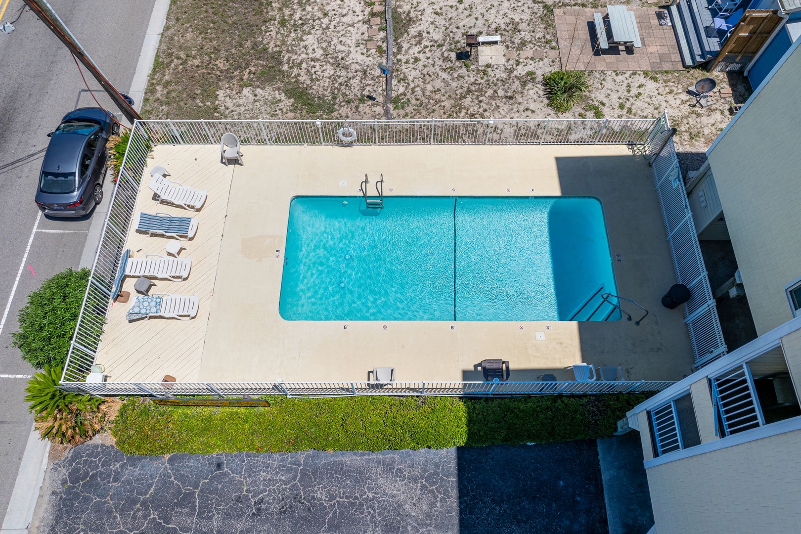 Aerial overview of the property's pool area, featuring a crisp rectangular pool with ladder access, surrounded by lounge chairs and gated deck space for outdoor relaxation.