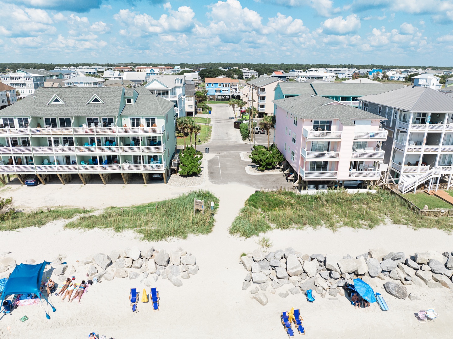 Aerial view of colorful beachfront properties lined along pristine sandy shores with beach umbrellas and loungers below.