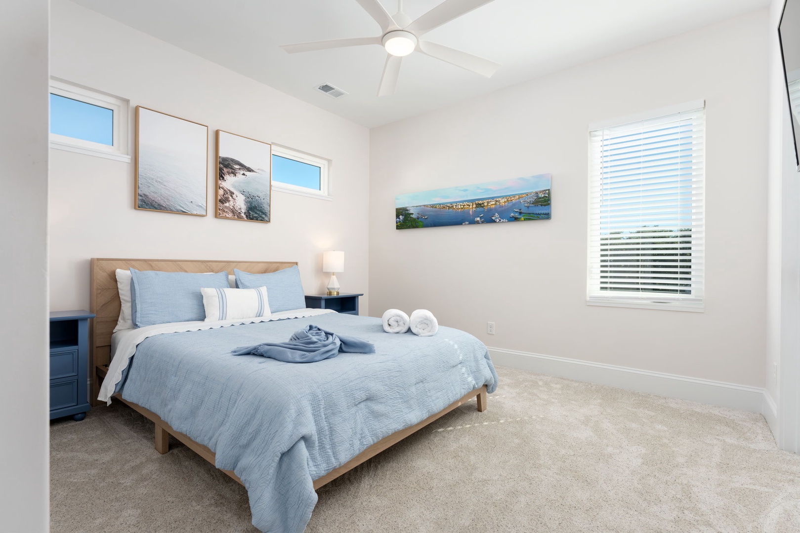 Unwind in your serene bedroom sanctuary with soft blue linens, coastal artwork, and gentle ceiling fan breezes creating the perfect retreat.