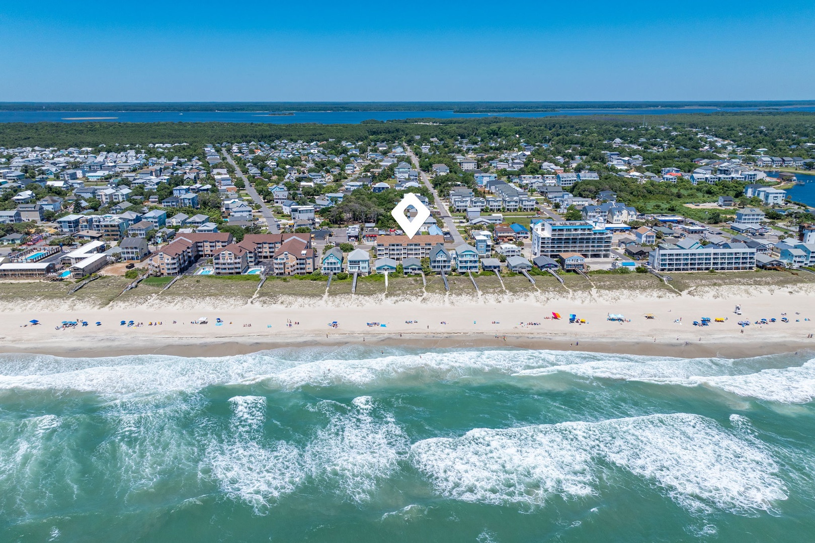 Aerial view of a beachfront community with turquoise waves rolling onto sandy shores, nestled between ocean and coastal waterways.