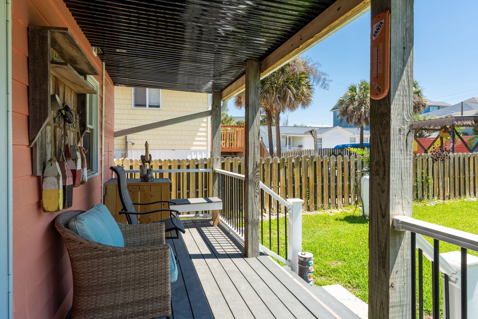 A covered deck with wicker seating faces palm trees and a lush green lawn, creating a peaceful outdoor retreat for your coastal getaway.