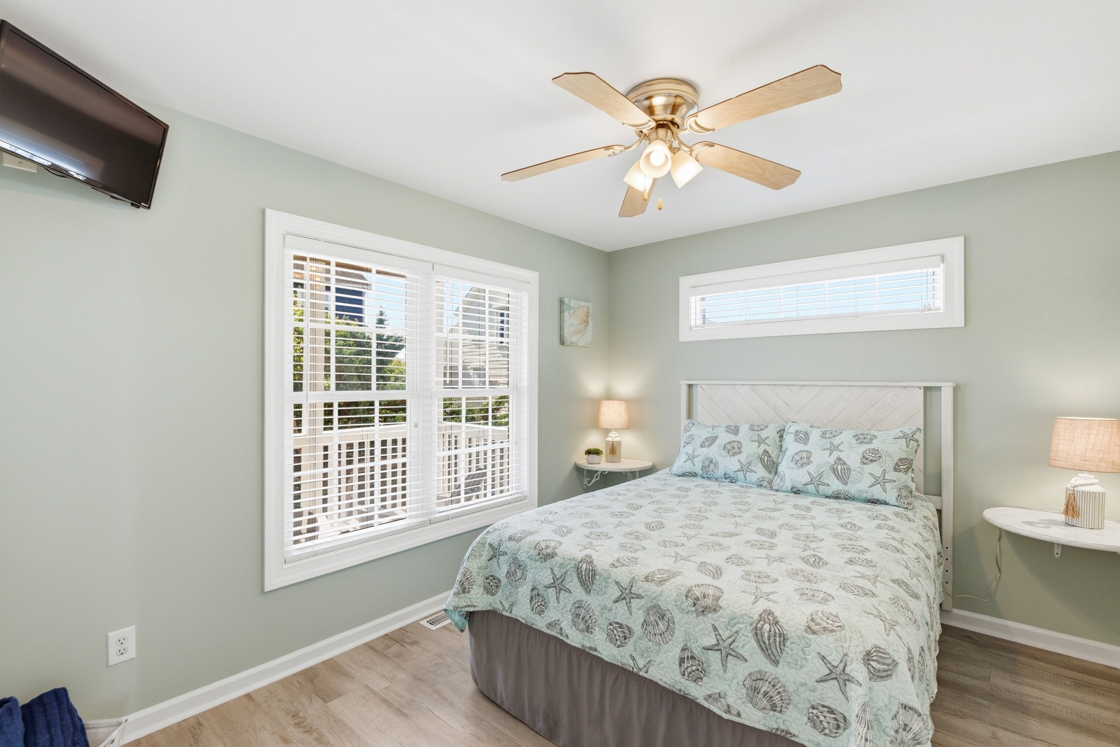 Drift off in this calming coastal bedroom, where soft sage walls and ocean-themed linens invite restful sleep. Natural light filters through plantation shutters while the ceiling fan keeps you comfortable year-round.