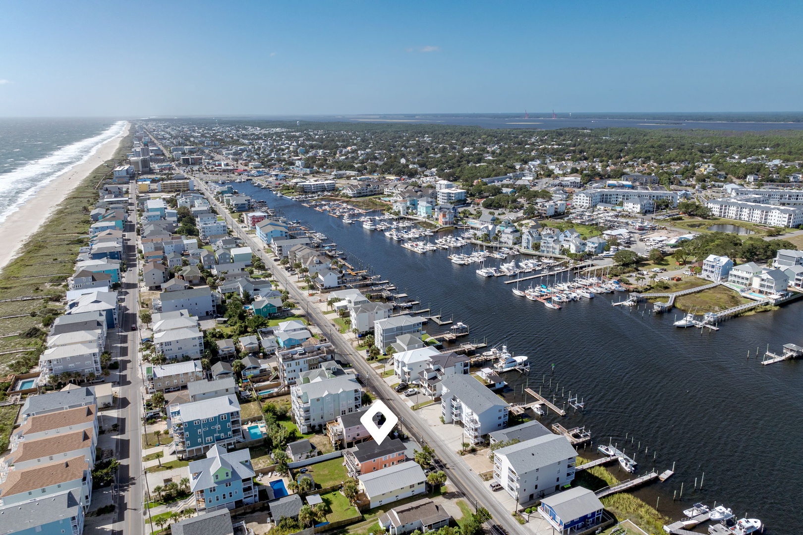 Aerial view of a charming coastal community featuring a pristine beach, bustling marina, and waterfront homes nestled between ocean and bay.